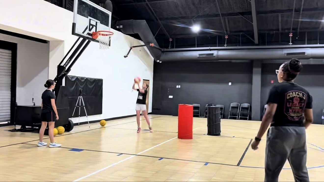 One of Coach J's players shooting at the basket while Coach J watches from the side of the court