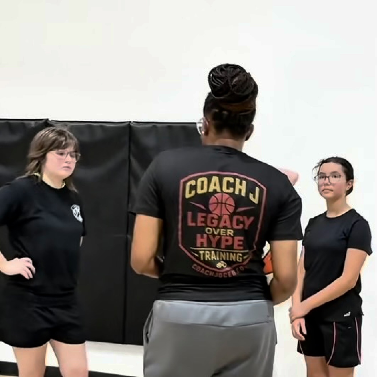 Coach J talking with two of her athletes in the gym, wearing her Legacy Over Hype training shirt