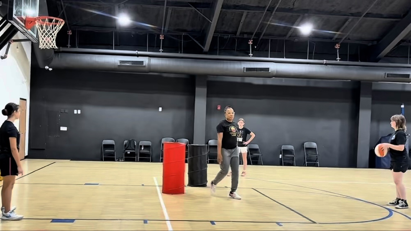 Coach J at center court during a training session, with training barrels set up and athletes on either side